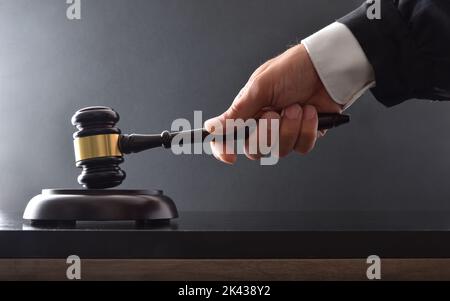 Mano che colpisce su base di legno con mazzuolo del giudice su tavolo nero e sfondo nero isolato. Vista frontale. Foto Stock