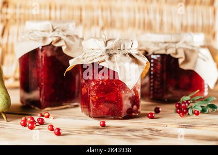 Vasetti di marmellata di lingoni e pere fatta in casa con carta artigianale su coperchi su superficie di legno accanto a bacche e pere fresche. Foto Stock