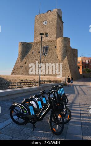 Termoli, Molise, Italia -08-29-2022- Bike elettrico condiviso stationl di fronte al castello svevo con una giovane coppia sullo sfondo Foto Stock