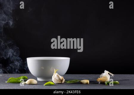 Chiudere il recipiente bianco con i fagioli di edamame e l'aglio con il vapore su fondo nero Foto Stock