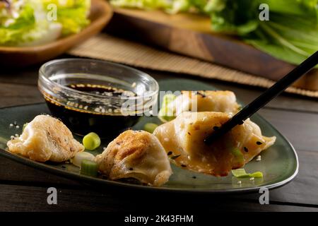 Primo piano di gnocchi asiatici, salsa di soia e bacchette con piatto e sfondo di legno Foto Stock