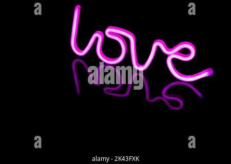 Immagine di un vivace testo amore al neon formato da bacchette rosa su sfondo nero e spazio copia Foto Stock