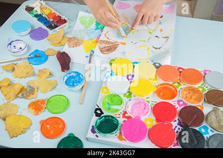 Bambino sta dipingendo e disegnando con acquerelli e colori delle dita. Stampa delle foglie sulla carta. Bambini che giocano, educano in belle arti. Bambini creatività. Foto Stock