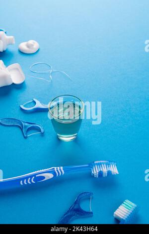 Immagine verticale di spazzolino da denti, dentifricio, filo e liquido sulla superficie blu Foto Stock