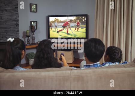 Vista posteriore della famiglia che si siede a casa e guarda una partita di hockey in tv. Sport, competizione, intrattenimento e tecnologia in composito digitale Foto Stock