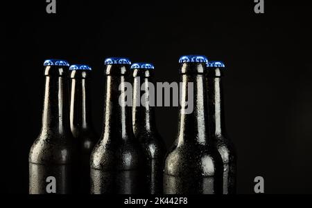 Immagine di sei bottiglie di birra con tappi a corona blu, con spazio copia su sfondo nero Foto Stock