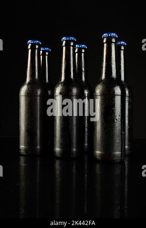 Immagine di sei bottiglie di birra con tappi a corona blu, con spazio copia su sfondo nero Foto Stock