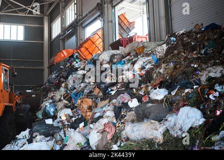 Un autocarro per rifiuti scarica i rifiuti domestici nella camera di ricezione di un impianto di smistamento rifiuti Foto Stock