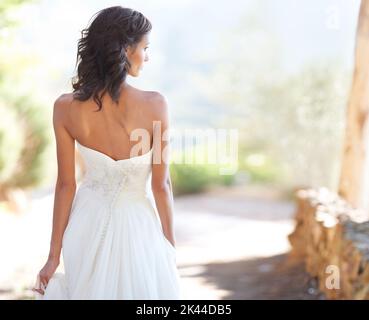 Camminando con orgoglio verso il futuro. Una giovane sposa che guarda di lato mentre percorre un sentiero all'esterno. Foto Stock