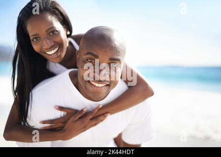 Theyre così nell'amore. Un bell'afro-americano che dà alla sua ragazza un piggyback sulla spiaggia. Foto Stock