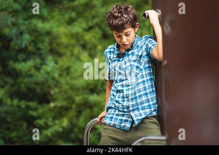 Un bambino si arrampica nel parco giochi per bambini del parco - un bambino esegue attività motorie all'aperto arrampicandosi sui picchetti al parco giochi all'aperto - p Foto Stock