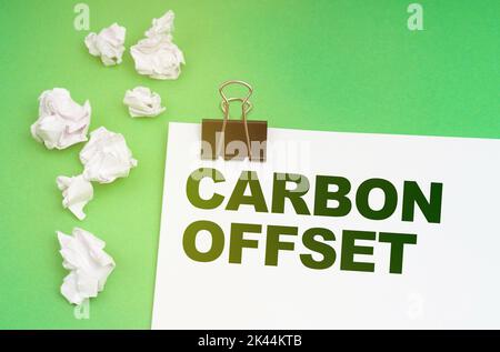 Concetto di ecologia. Su sfondo verde, carta stropicciata e un foglio con l'iscrizione -offset carbonio Foto Stock