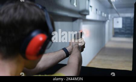 Sparatutto uomo che tiene la pistola in mano e sparare a un bersaglio vista posteriore Foto Stock