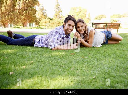 Condividere una bibita nel parco. Una giovane coppia felice che sorseggia una cola nel parco. Foto Stock