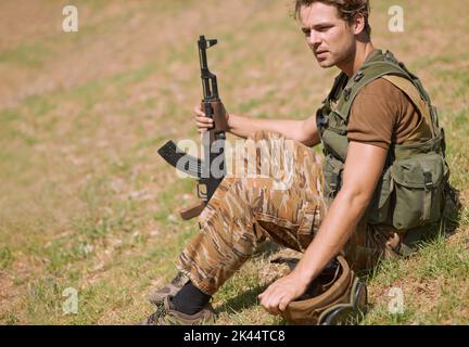 Dietro le linee nemiche. Un giovane soldato seduto sull'erba fuori. Foto Stock