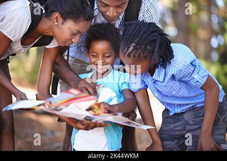 Perdersi è metà del divertimento: Una famiglia felice che legge una mappa insieme mentre si fa un'escursione nei boschi. Foto Stock