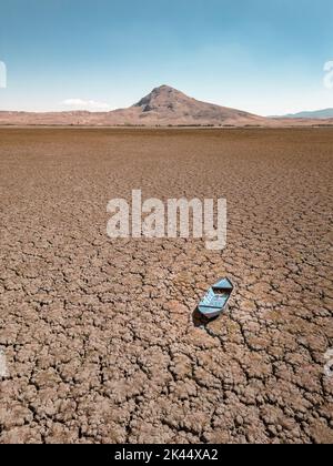 Barca a remi abbandonata su terreno incrinato sul letto del lago seccato a causa del riscaldamento globale e della siccità Foto Stock