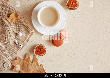 Stile di vita casual femminile - maglione bianco e cuffie. Tempo di caffè estetico tra foglie autunnali, amaretti e fichi con spazio copia. Foto Stock