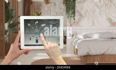 Sistema di controllo della casa con telecomando intelligente su un tablet digitale. Dispositivo con icone app. Camera da letto in legno bohémien in stile bohémien. Letto matrimoniale sullo sfondo, arco Foto Stock