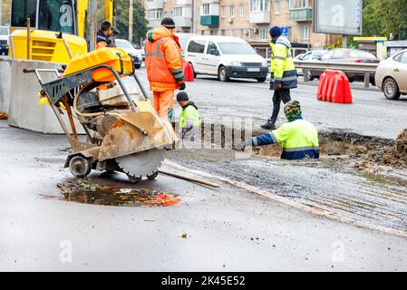 Un gruppo di lavoratori della strada ripara i portelli delle fognature e cambia vecchi tombini in cemento per nuovi su una strada in un giorno di autunno. Foto Stock