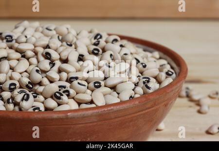 Piselli secchi neri secchi non cotti in ciotola su tavola di legno Foto Stock