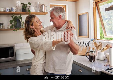 Donna anziana e uomo che ballano in cucina, godendosi il loro pensionamento. Amore, famiglia e felicità per anziani, pensionati e felice coppia che hanno un Foto Stock