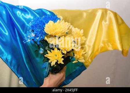 La ragazza sta tenendo fiori patriottici blu-gialli di fronte alla bandiera nazionale dell'Ucraina. Famiglia, unità, sostegno. Spazio di copia Foto Stock