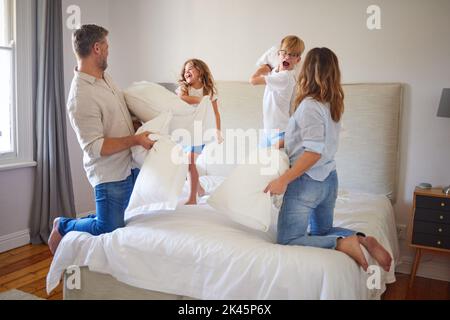 Lotta cuscino famiglia, in camera dei genitori e i bambini sorridono con felicità. I bambini saltano su un letto, giocando con mamma e papà a casa. Buon tempo di legame Foto Stock