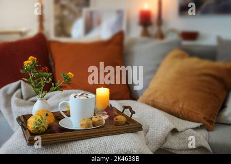 Relax con cioccolata calda su un vassoio con candele e decorazione autunnale sul divano in un accogliente soggiorno, spazio copia, focus selezionato, profondità stretta Foto Stock
