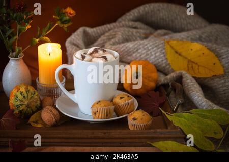 Cioccolata calda con marshmallows, servita con muffin, candele e decorazioni autunnali su un caldo e accogliente sfondo scuro, spazio copia, selecte Foto Stock