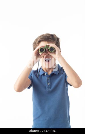 Ragazzo caucasico in T-shirt blu guardando la macchina fotografica con espressione sorpresa attraverso binocoli, su sfondo bianco. Foto Stock