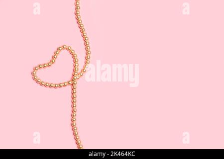 Forma a cuore realizzata con collana in perla su sfondo rosa con spazio copia Foto Stock