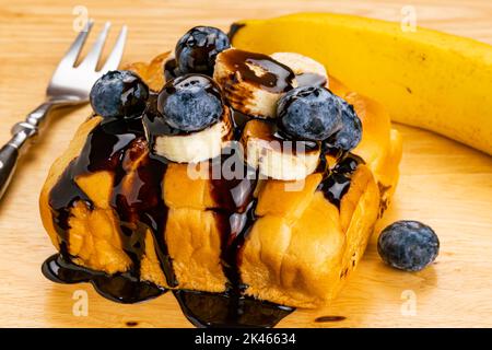 Vista dall'alto del delizioso pane fatto in casa con banana sbucciata a fette e mirtillo biologico versato con sciroppo di cioccolato con banana matura intera Foto Stock