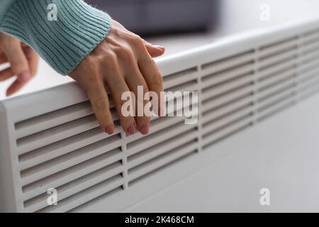 Mano della donna su un radiatore bianco. Stagione di riscaldamento. Crisi energetica. Batterie fredde. Riscaldamento centralizzato Foto Stock