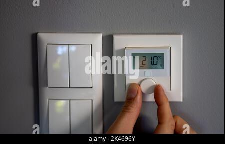 La mano modifica la temperatura a 21 gradi Celsius su un termostato elettronico. Simbolo per il risparmio energetico. Foto Stock