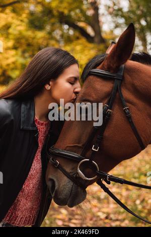 Bella donna brunetta baciare un cavallo nella foresta autunnale Foto Stock