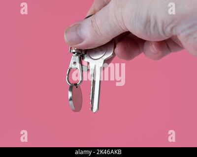 persona che tiene la chiave della porta anteriore ad un nuovo proprty isolato su uno sfondo rosa Foto Stock