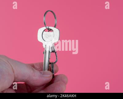 agente che tiene la chiave della porta anteriore su un anello portachiavi fuori di una nuova casa isolata su uno sfondo rosa Foto Stock