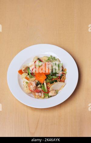 Mescolate le tagliatelle fritte con i frutti di mare e sistemate su un piatto bianco, su un tavolo di legno Foto Stock