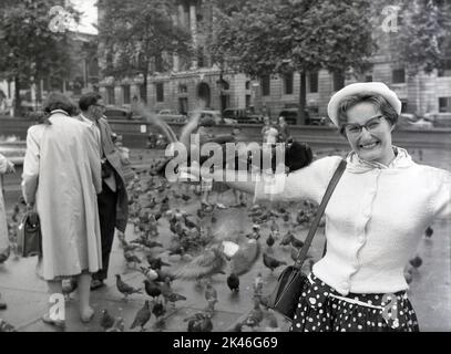 1958 piccioni storici seduti su un braccio estensivo di una signora eccitata a Trafalgar Square, Westminster, Londra, Inghilterra, Regno Unito. Nella sua mano una piccola scatola di piselli. Foto Stock