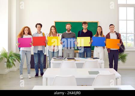 Gli studenti sorridenti e il loro insegnante di sesso maschile che tiene poster di carta colorati con spazio per il testo Foto Stock