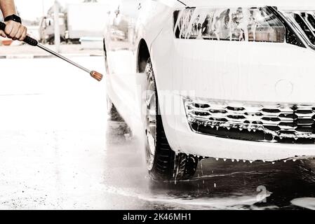 La mano di un uomo lava la sua auto bianca al lavandino. Sapone su un'auto Foto Stock