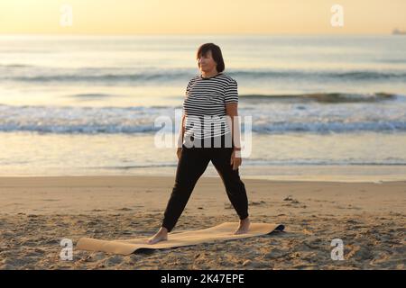la donna di mezza età si prende cura del corpo e fa yoga al mare all'alba al mattino. Donna vestito l'abbigliamento sportivo e fare sport ex Foto Stock