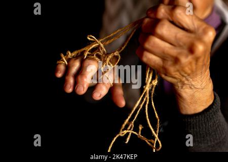 Mani di vecchia donna con malattia di poliartrite. Corde di tela sulle dita della signora anziana, marionette. Foto di alta qualità Foto Stock