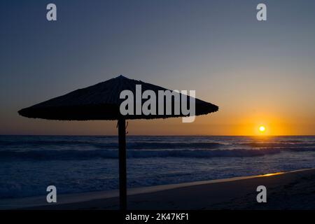 Una silhouette ombrello durante il tramonto sulla spiaggia di Vrahos. Foto Stock