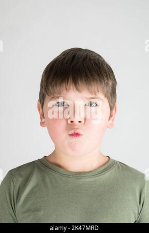 Ragazzo, ritratto di sei anni. Bambino che fa la grimace. Sfondo bianco. Verticale orizzontale. In camicia verde. Foto Stock