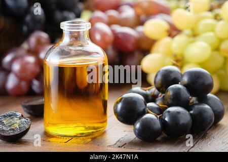 Bottiglia di olio essenziale per semi d'uva biologici. Uve nere, verdi e viola in tavola. Foto Stock