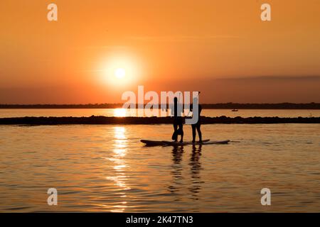 Silhouette di un uomo con una pagaia su una tavola da surf SUP al tramonto di Odessa. Pittoresco corpo d'acqua la sera. Tema di uno stile di vita attivo Foto Stock