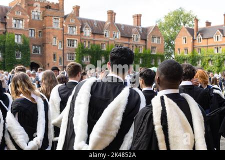 Vista posteriore di studenti universitari britannici e africani freschi di sesso maschile e femminile con abito e indirizzo accademico a piedi nel campus universitario, Cambridge, Regno Unito durin Foto Stock