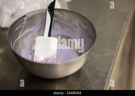 chef che prepara per glassa una torta all'acqua lilla nel laboratorio professionale della cucina Foto Stock